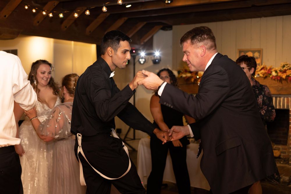Wedding guests dancing energetically at a reception with string lights in the background.