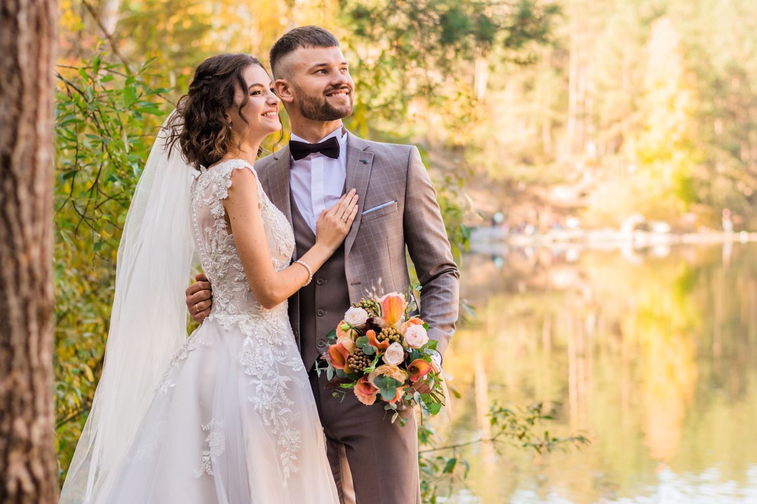 A romantic autumn wedding couple embracing by a serene lake with golden light.