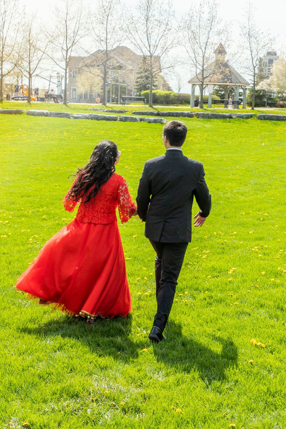 Bride and groom (bride wearing traditional red dress)  running together in a field
