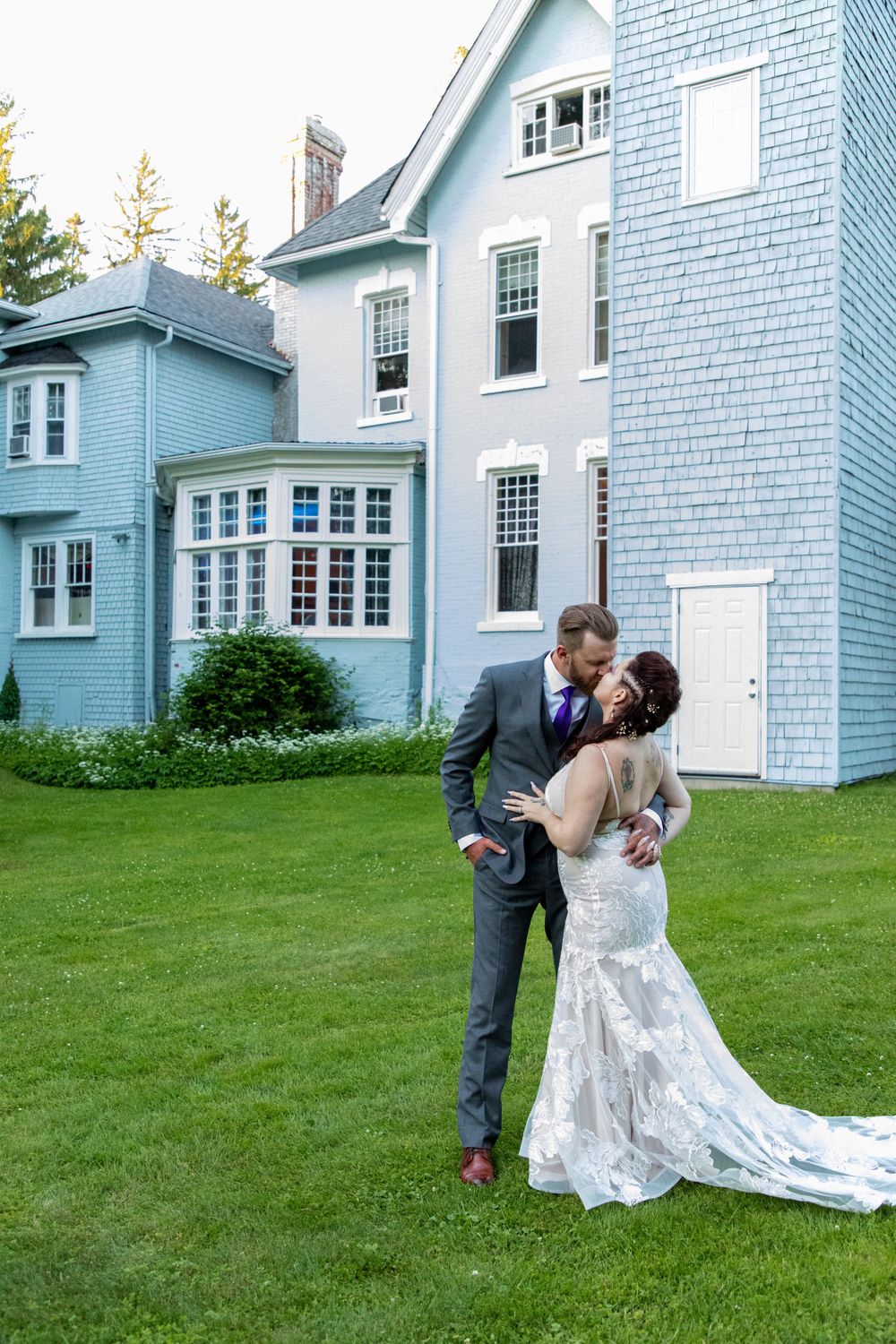 A bride and Groom kissing in front of the blue main building at The Sir William Mackenzie Inn