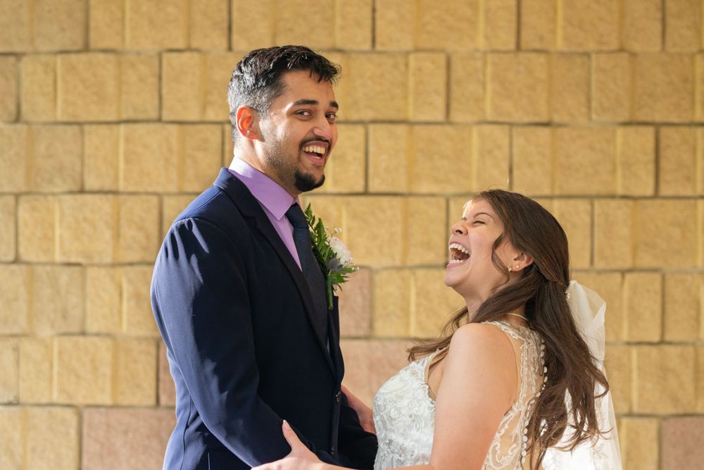 A bride and groom holding each others arms laughing