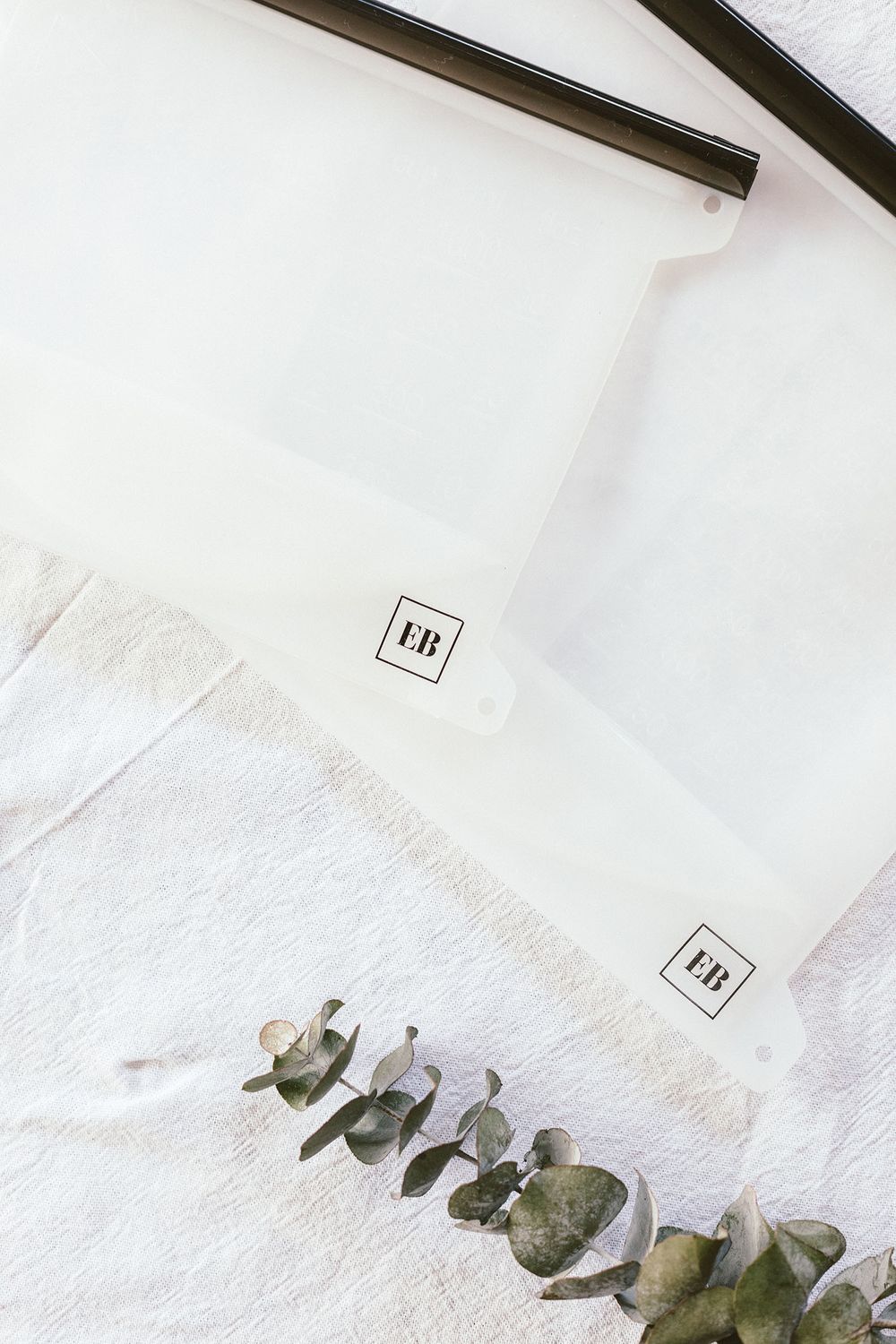 Minimalist white storage bags with black seals and eucalyptus leaves on white background.