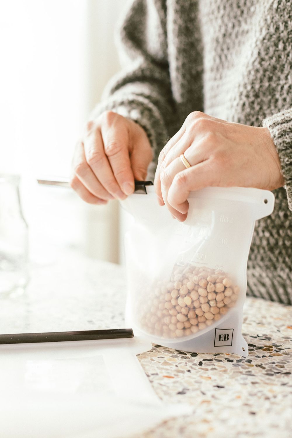 Hands sealing a reusable storage bag filled with chickpeas.