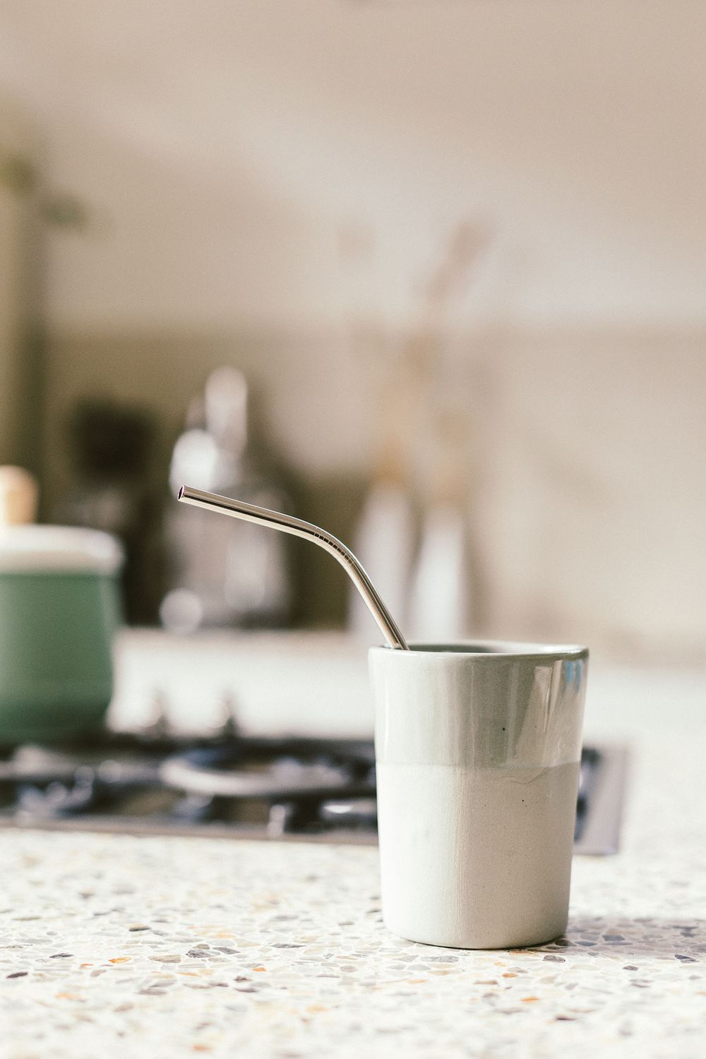White ceramic cup with metal straw on speckled countertop.