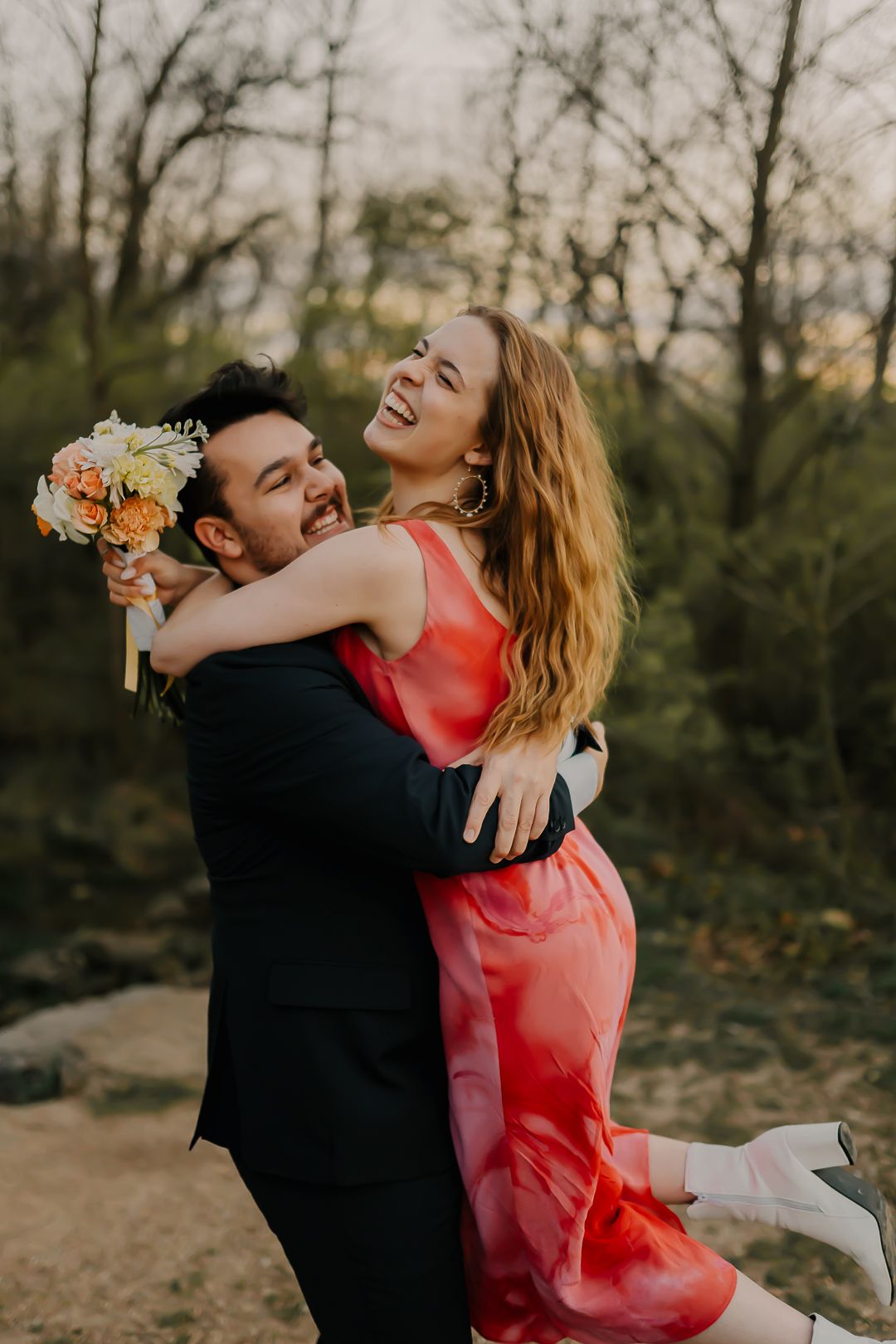 Romantic couple in formal wear embracing outdoors during sunset photoshoot.