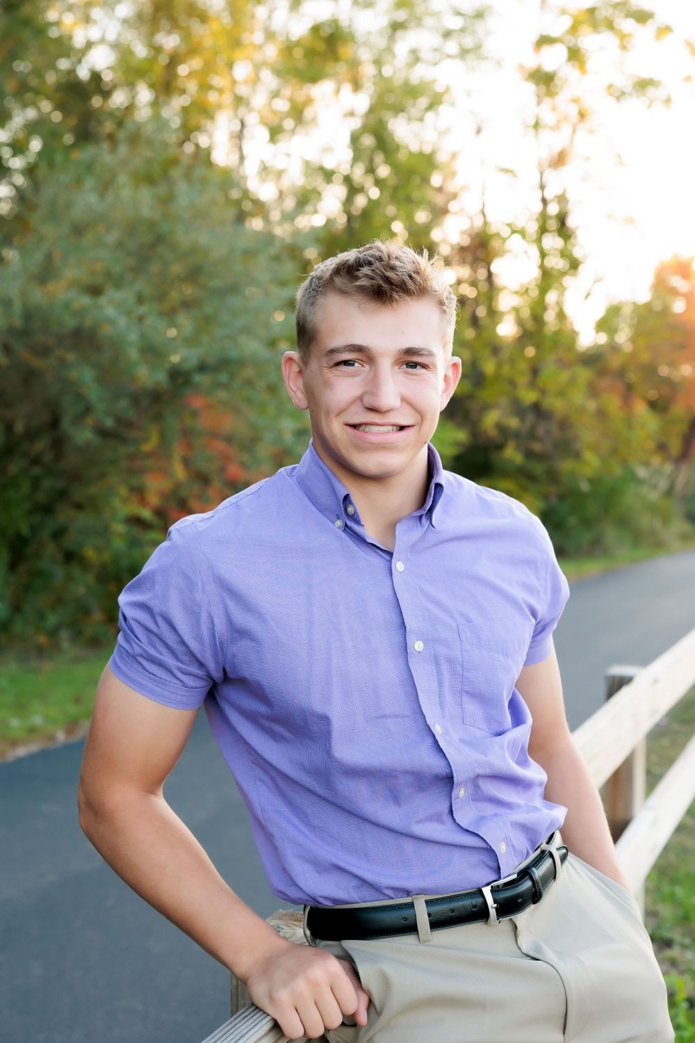 Person wearing light purple shirt leans against white railing on path.