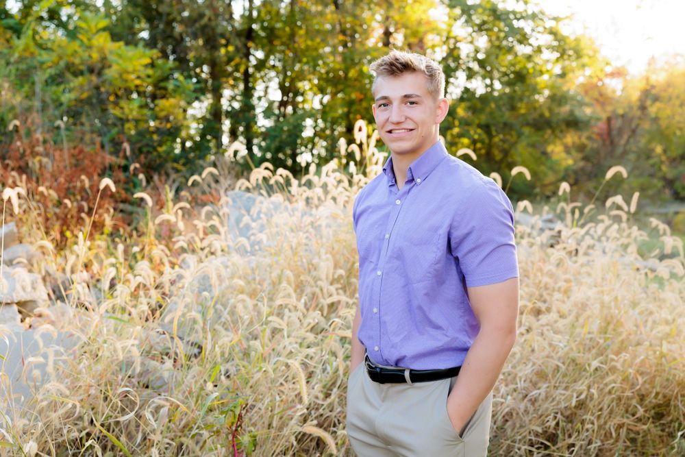 Person in lavender shirt stands in golden field during sunset.