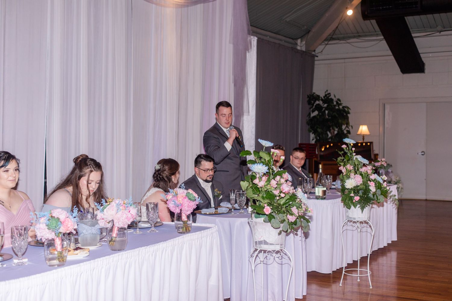 Wedding reception venue setup with head table and white drapery decorations.