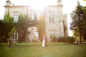 Golden sunlight illuminates a historic stone mansion with couple on the lawn.