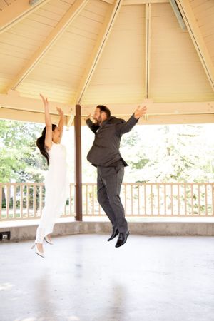 Groom performs playful jumping sequence in covered outdoor pavilion during wedding celebration.