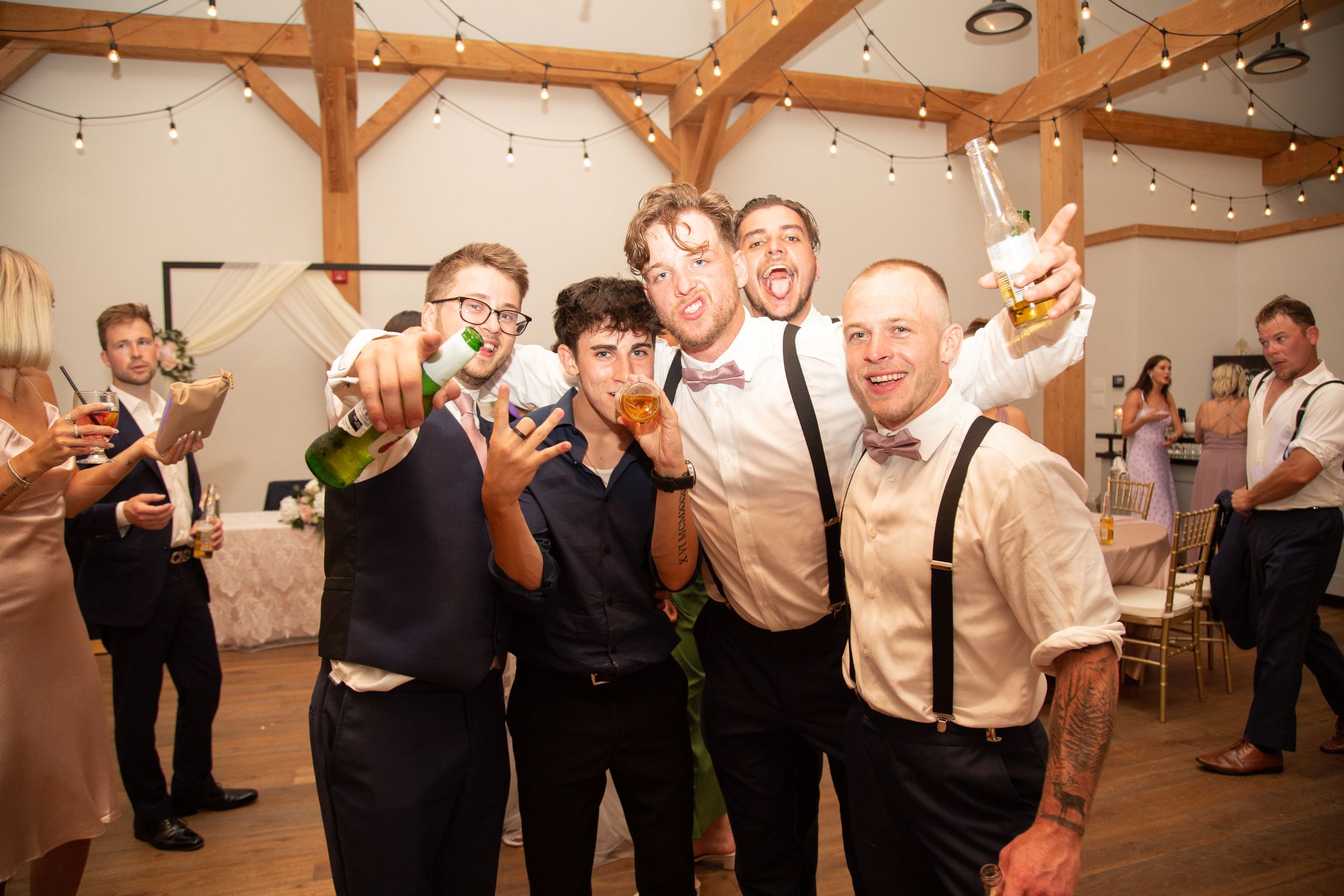 Groomsmen celebrating at a wedding reception with drinks in a rustic barn venue.