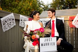 A wedding couple sits together with a 'Just Married' sign and papel picado decorations.