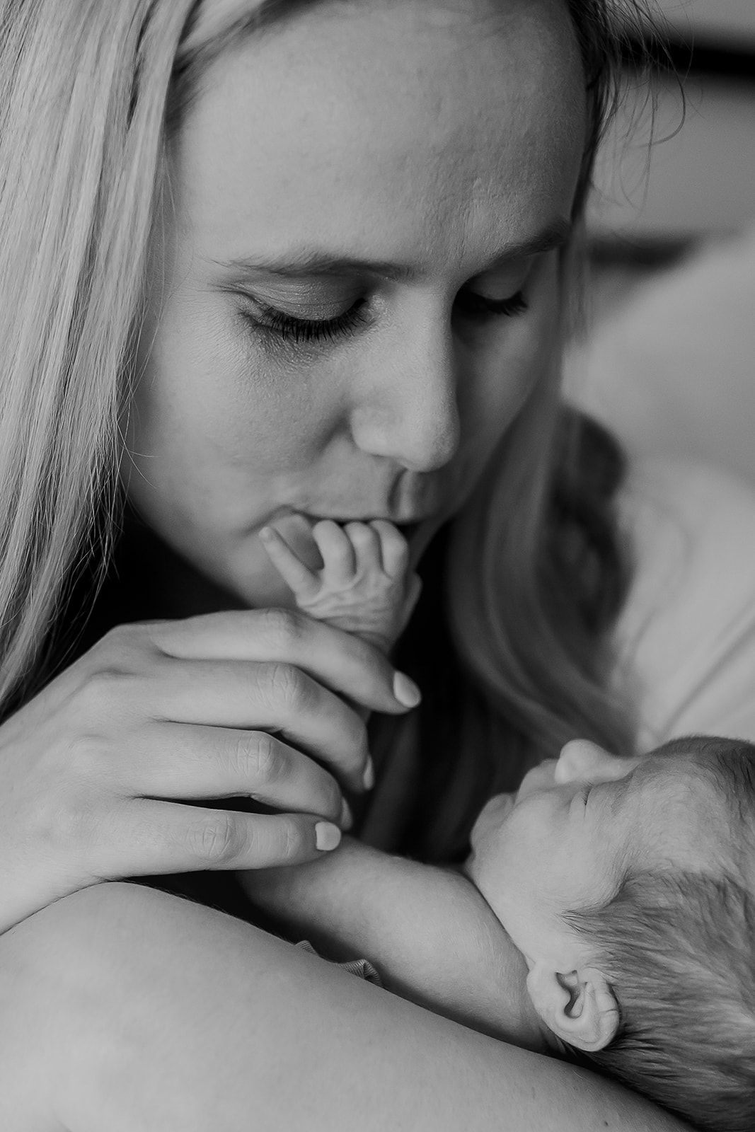 A black and white image of a mom kissing her newborn son's fingers.