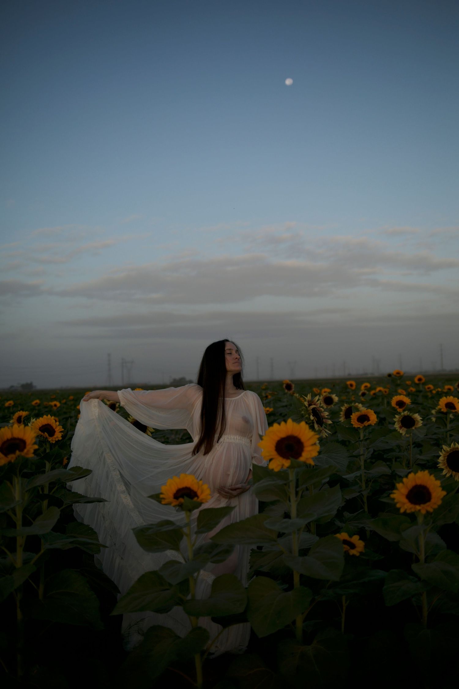 Figure in flowing white dress dancing through sunflower field at dusk.