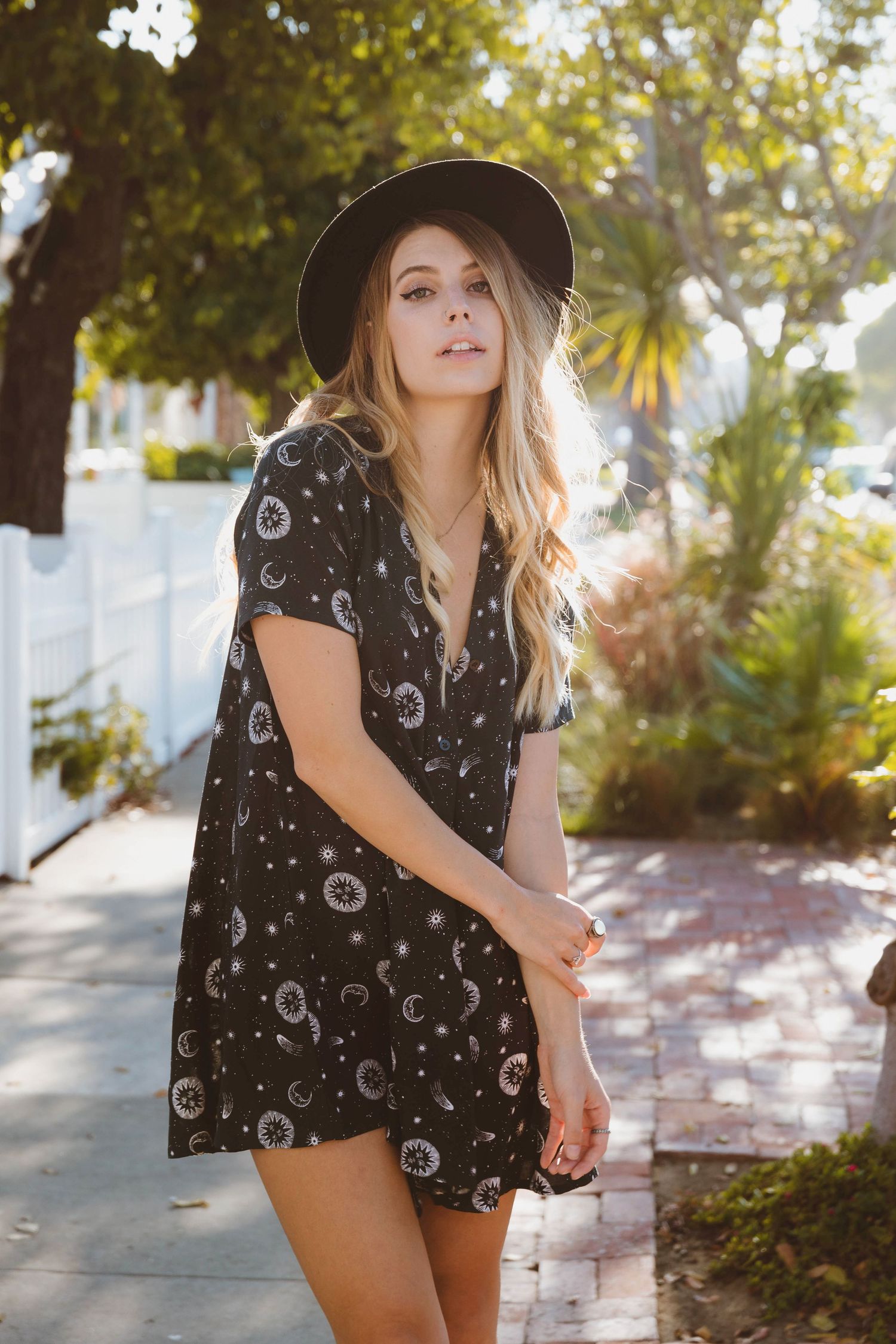 Boho style portrait in patterned dress and hat on sunny suburban sidewalk.