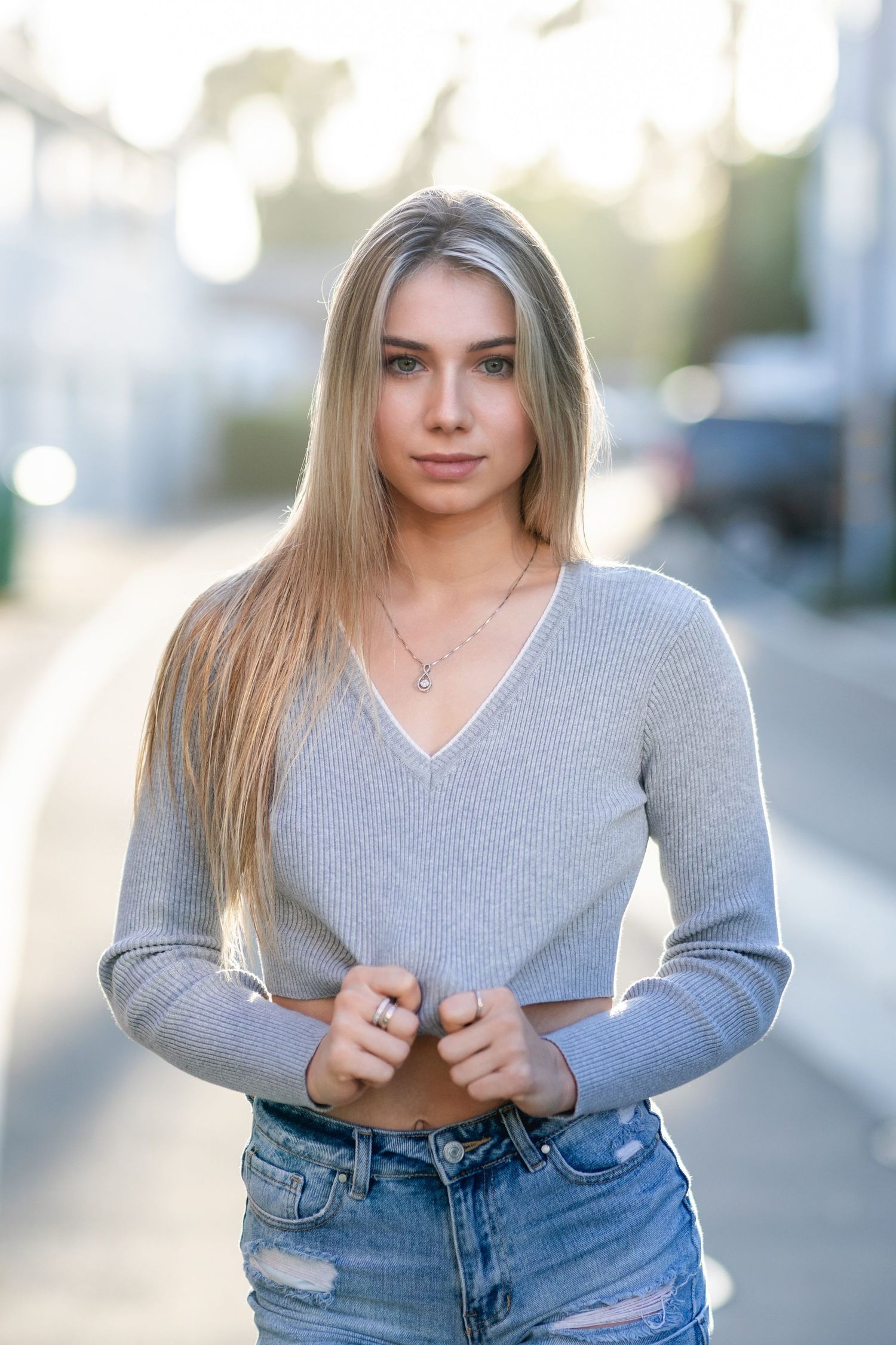 Street style portrait in grey v-neck sweater and distressed denim with soft bokeh background.