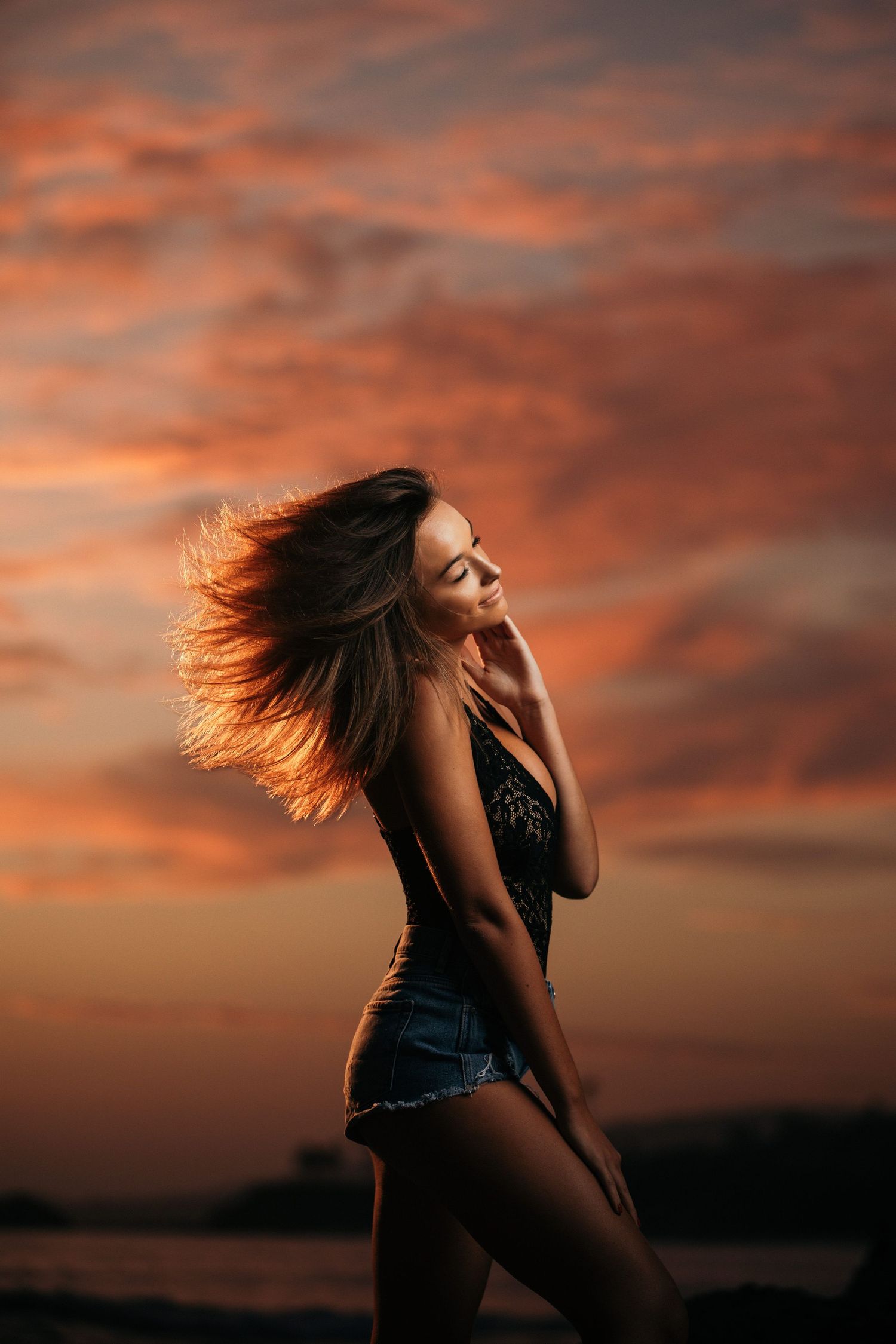 Dramatic silhouette of woman with flowing hair against vibrant orange sunset sky.