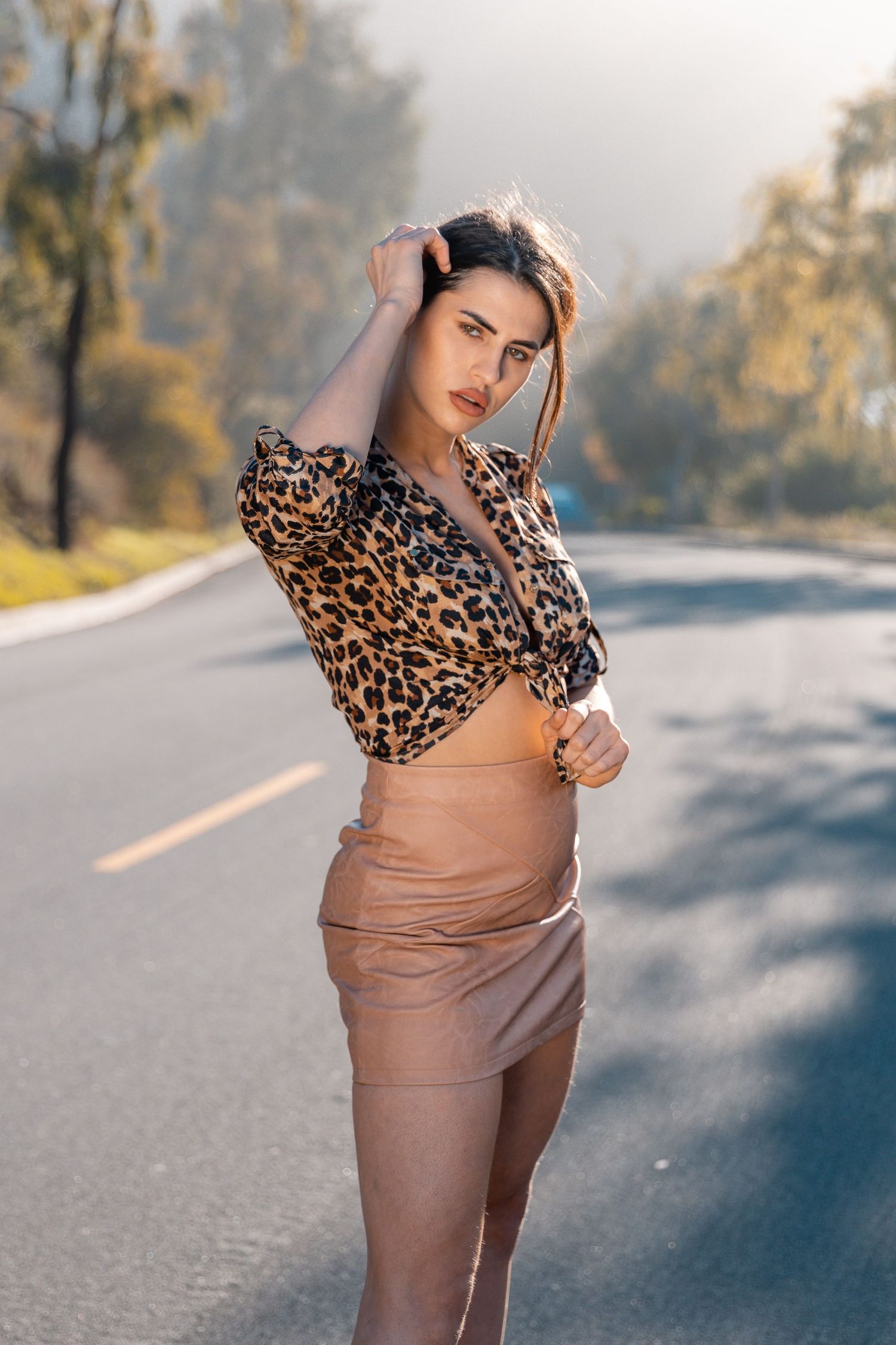 Fashionable outfit featuring leopard print top and tan skirt on a sunlit road.