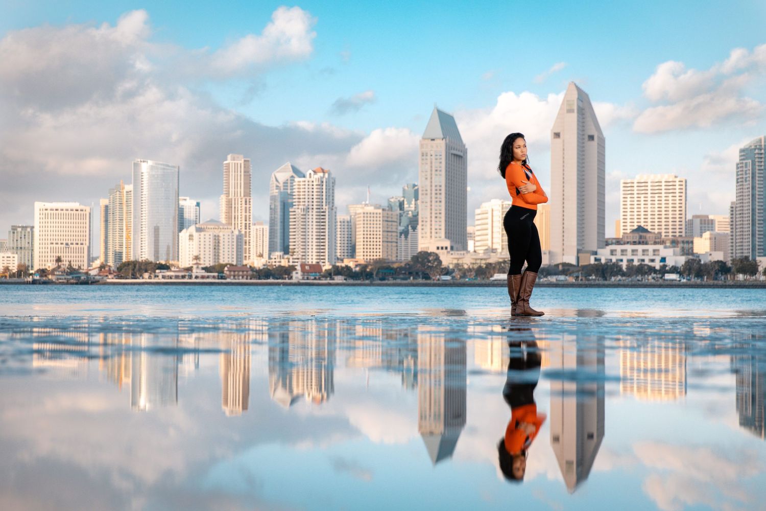 Athletic silhouette reflected in water against San Diego skyline during sunset with dramatic clouds.