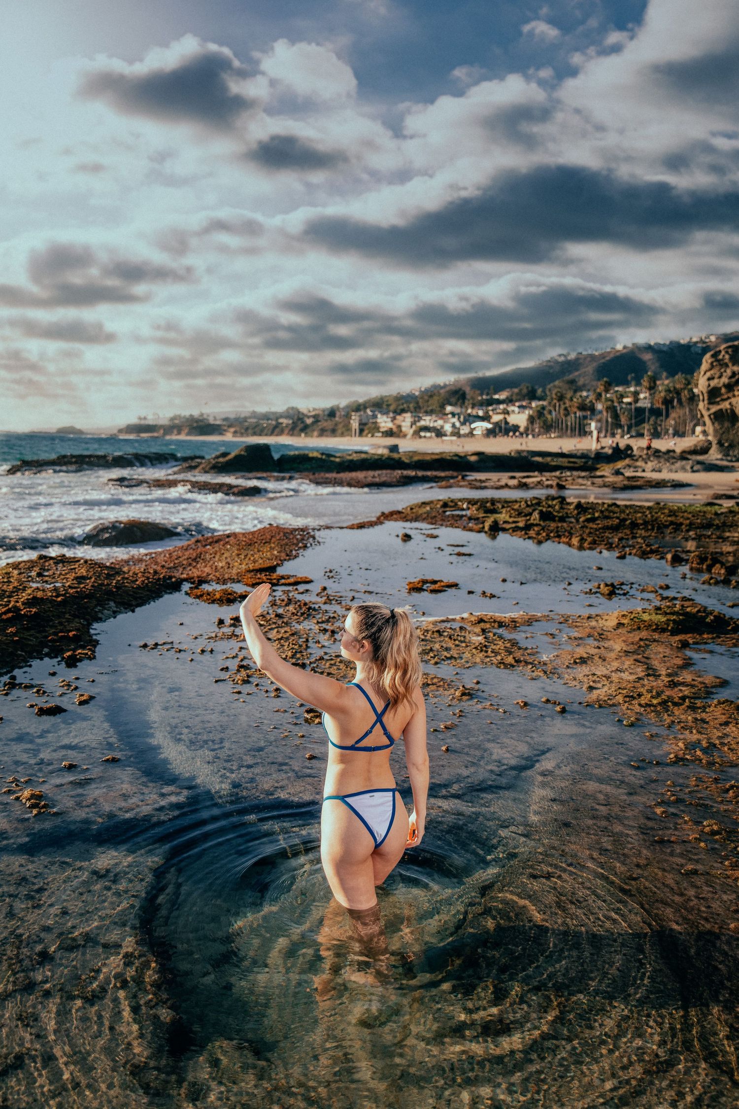 Woman wading in coastal tide pool during dramatic cloudy sunset.
