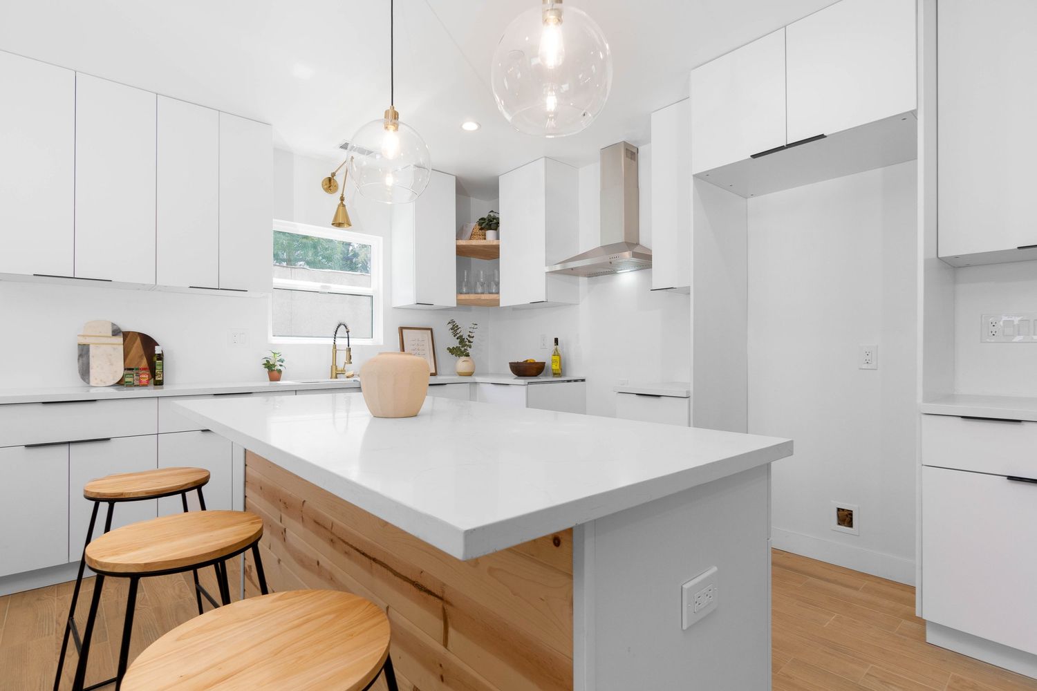 Bright white kitchen with wood accents, pendant lighting, and modern waterfall island counter.