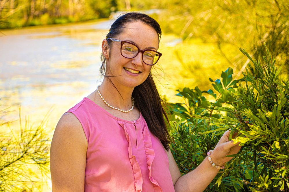 Person in pink sleeveless top smiling while standing in natural outdoor setting.