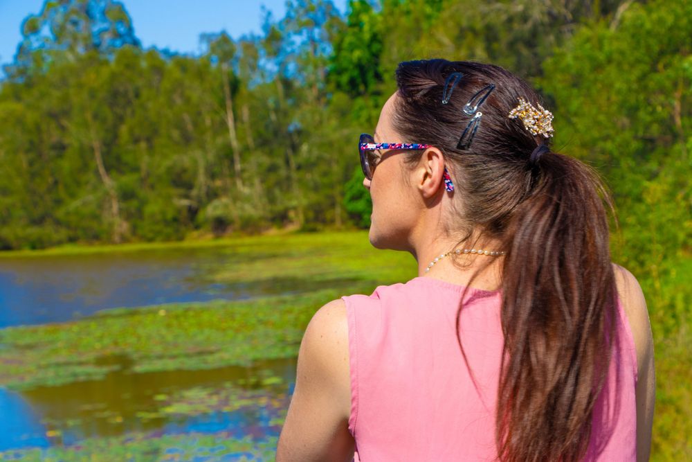 Person in pink sleeveless top enjoying view of pond with lily pads on sunny day.