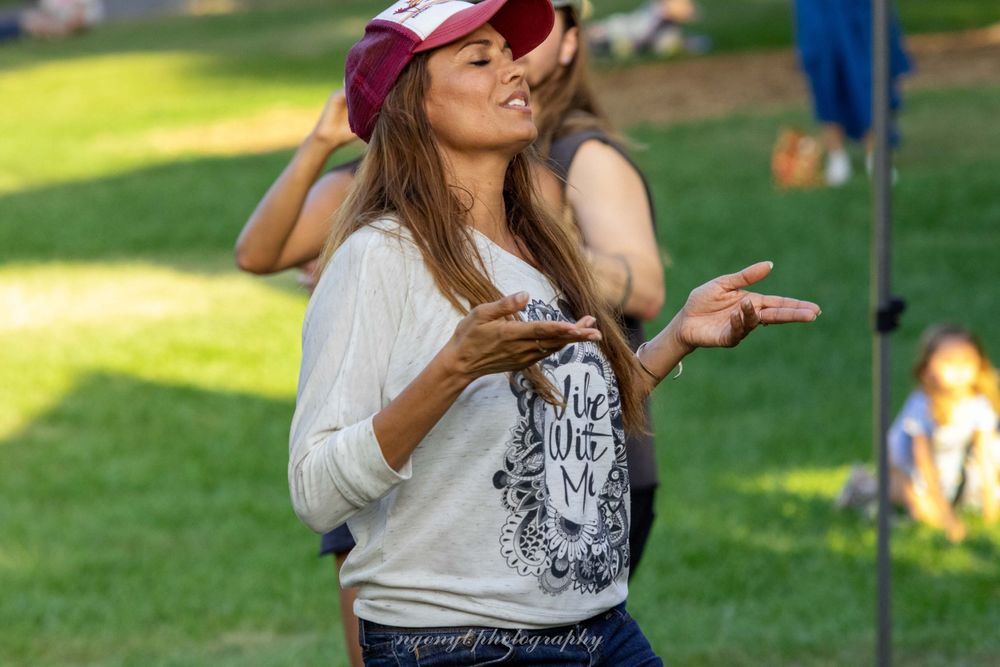 Dancing figure wearing a red cap and white shirt enjoys music in a park.