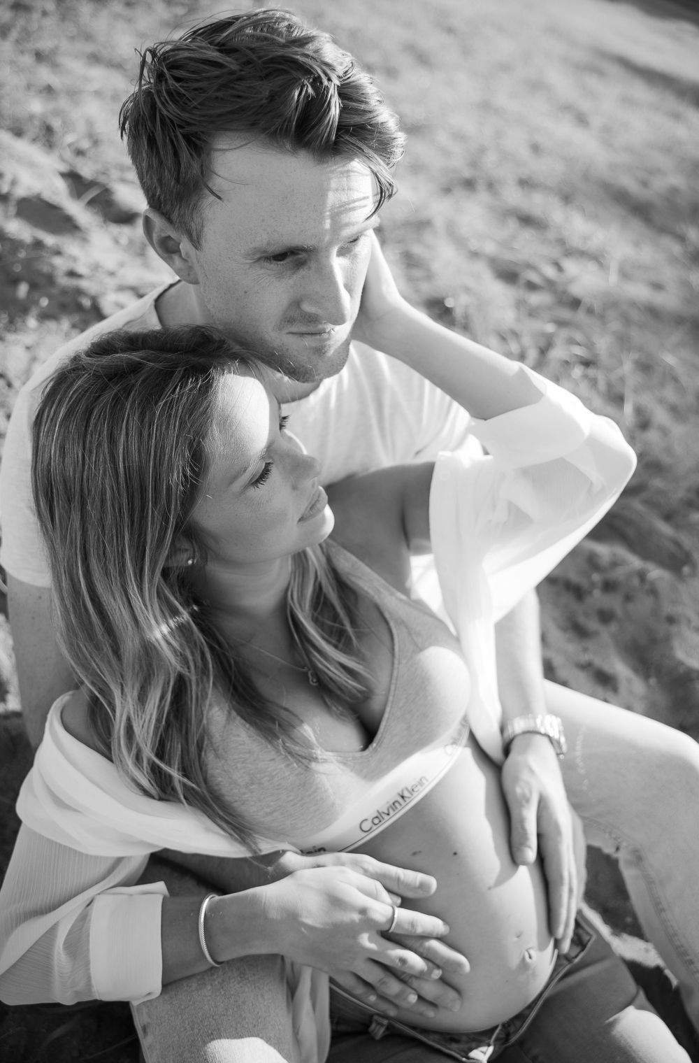 pregnant woman wearing calvin klein bra set sitting against man holding her belly on South Beach in Staten Island