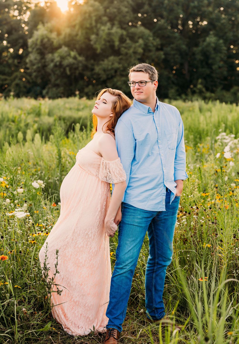 Maternity couple with woman leaning against the back of man in sun soaked flower field in Staten Island, NY