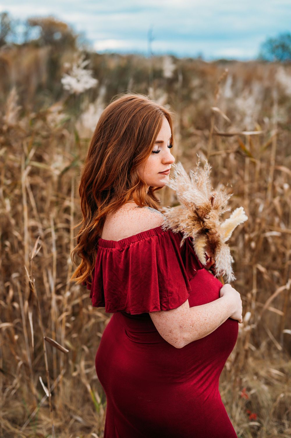 pregnant woman wearing red holding pampas grass in dried field in Staten Island, NY