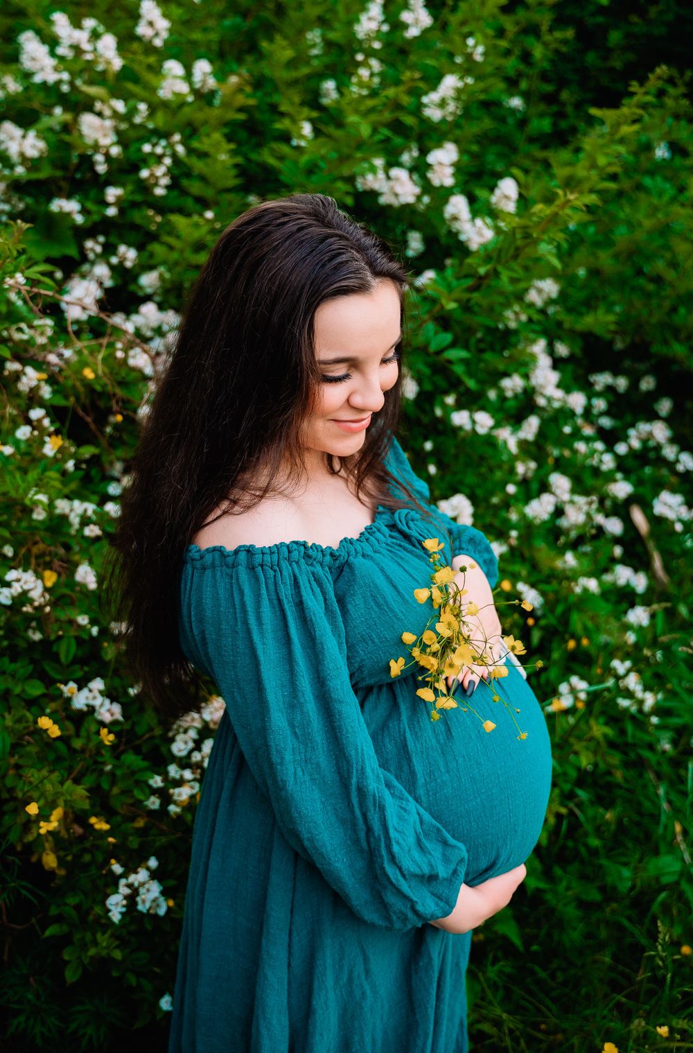 Pregnant mother holding yellow flowers against her belly in white floral field in Staten Island, NY