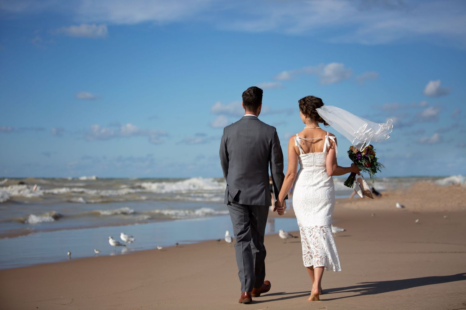 Newlyweds walking along beach shoreline with flowing veil.