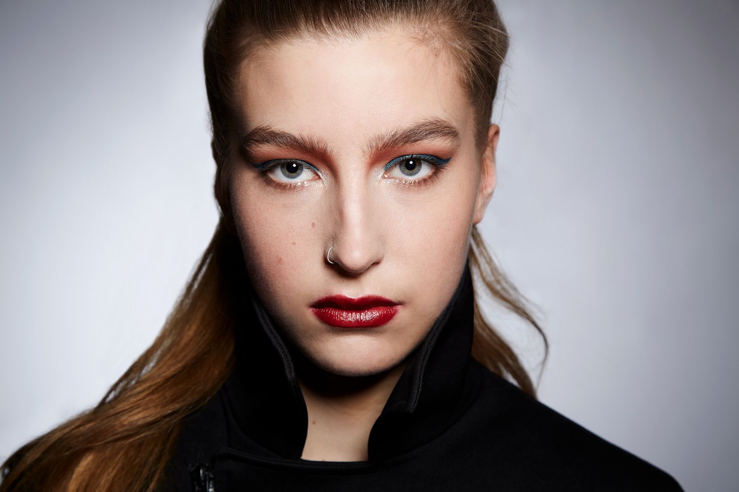 Close-up beauty portrait showcasing bold red lipstick and sleek hair against gray background with dramatic lighting.