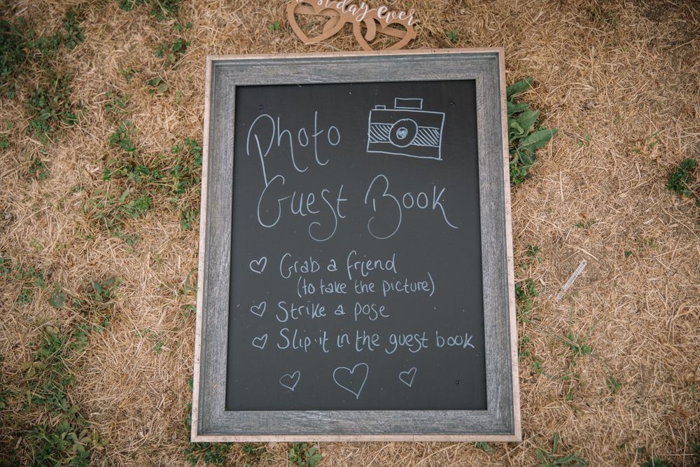 A chalkboard sign displaying photo guest book instructions at an outdoor event.