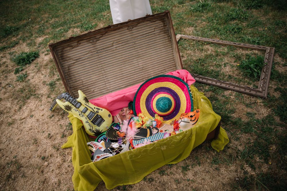 A vintage suitcase filled with colorful props and party accessories displayed on grass.