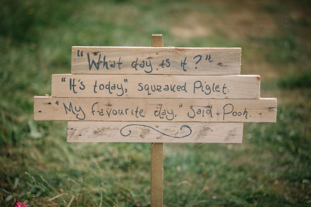 A rustic wooden sign with handwritten text displayed in an outdoor garden setting.