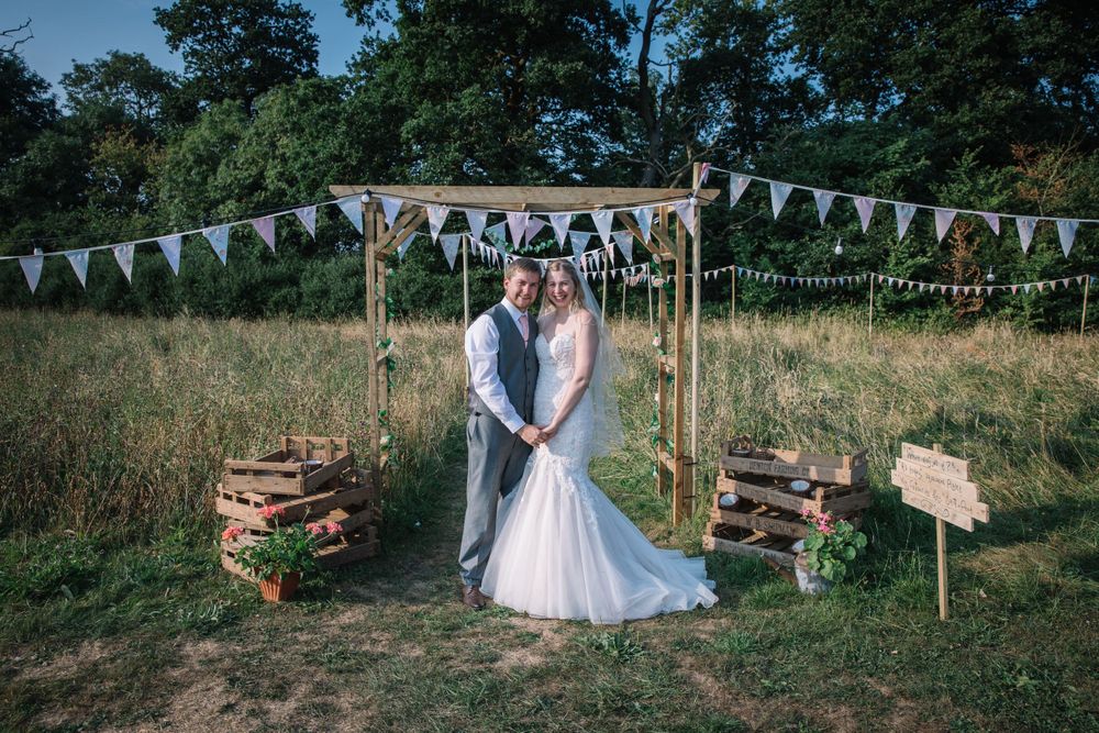 A wedding arch decorated with white bunting flags and rustic wooden crates in a meadow setting.