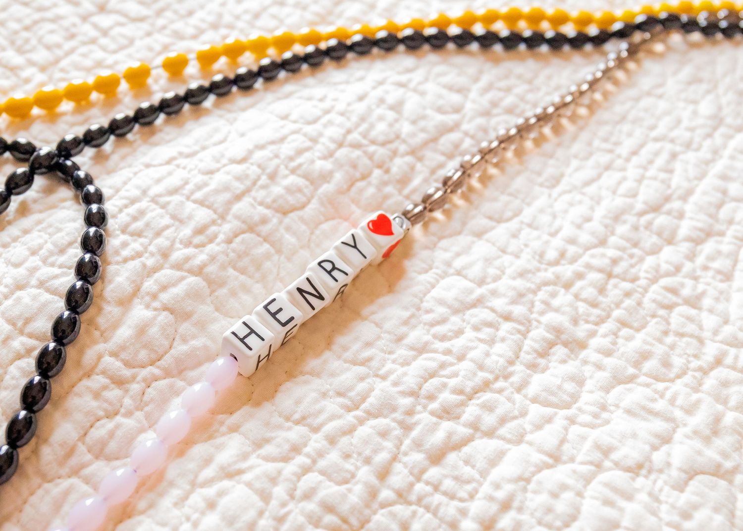 Beaded necklace with letter beads spelling 'HENRY' on white textured background.