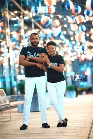 Couple in coordinated black shirts and white pants embrace under festive lighting.