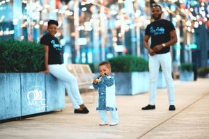 Family wearing matching outfits poses on urban walkway with decorative lights.