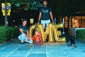 Family photo with large gold LOVE balloons outdoors at night.