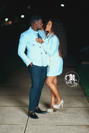 Romantic couple in matching white outfits pose under evening lights.