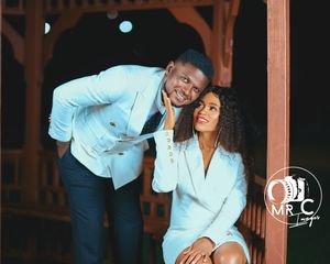 Intimate portrait of couple in light colored outfits under wooden structure.