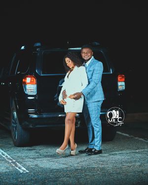 Couple in coordinated formal wear pose together against black SUV at night.