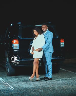 Elegant couple posing in formal wear by black SUV at night.
