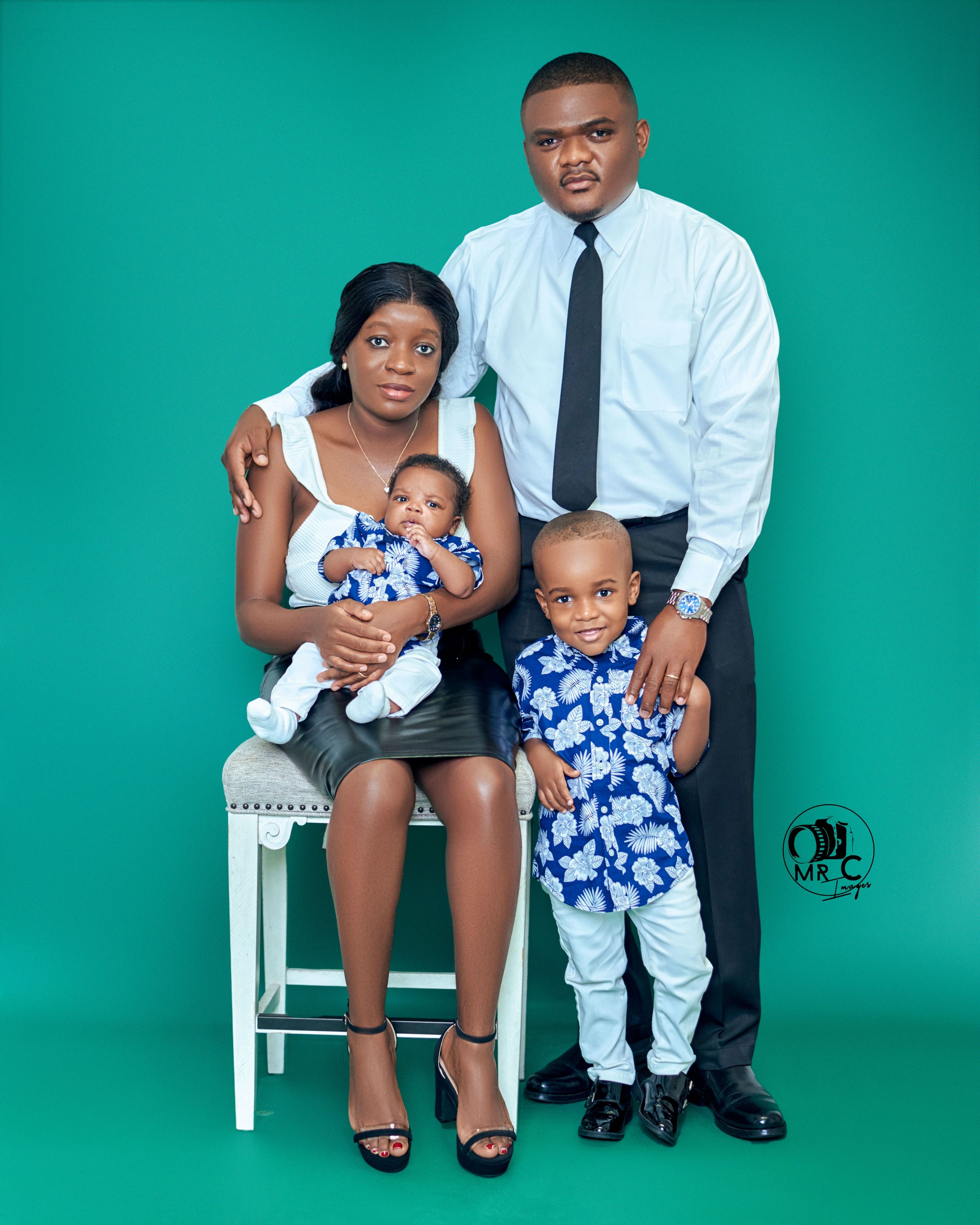 Family of four poses in coordinated outfits against a teal background for formal portrait.