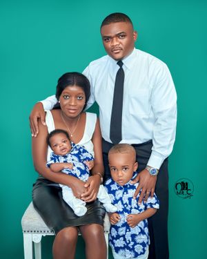 Family portrait with parents and two children in coordinated blue and white outfits against teal background.