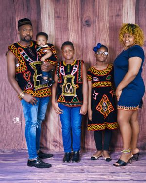 Family wearing coordinated African print outfits posing against wooden wall background.