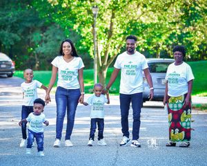 Family wearing matching white t-shirts walking together on a tree-lined path.